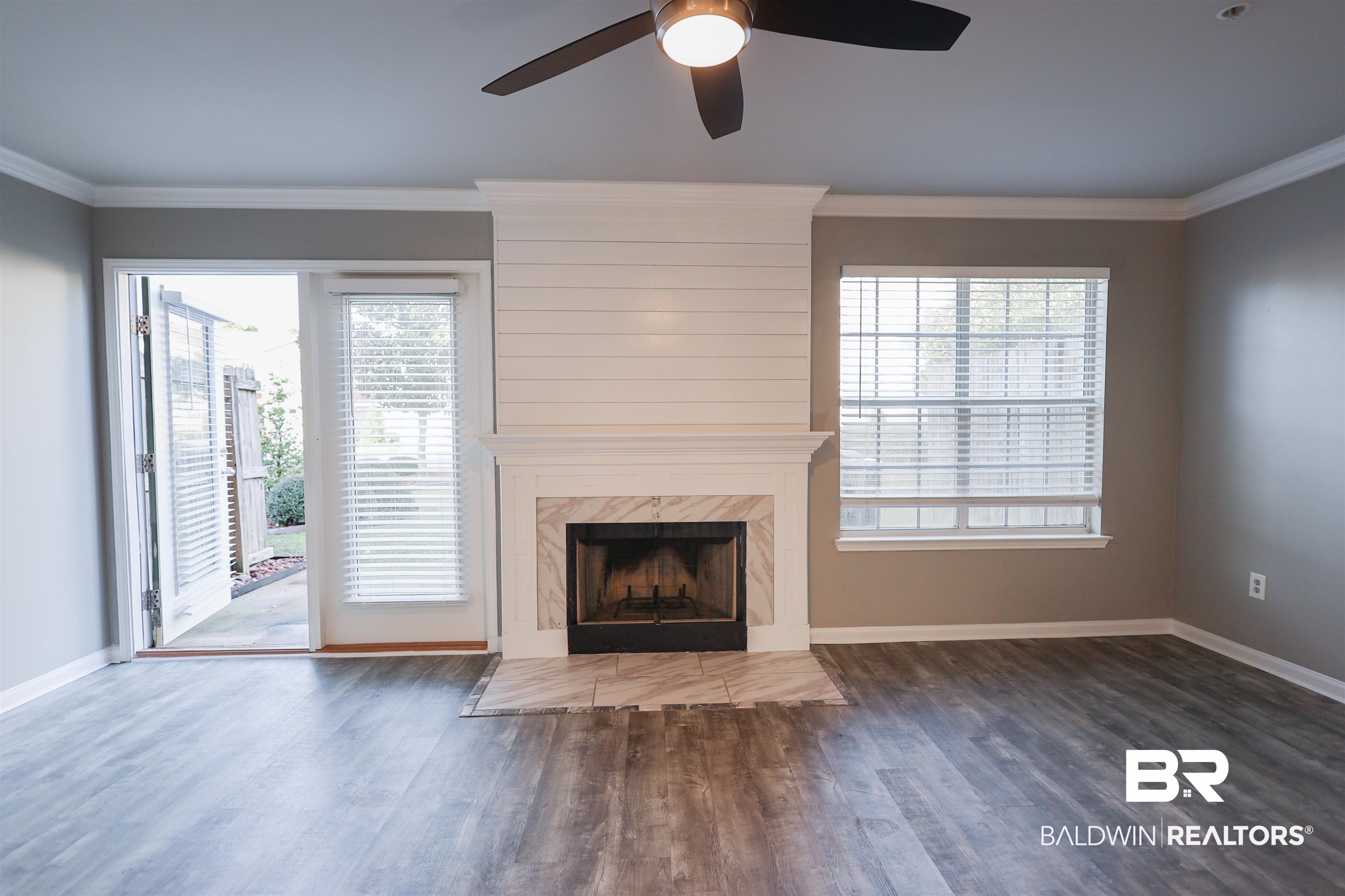 1517 Regency Road, Unit 125 Gulf Shores, AL 36542 - Photo 4 of 26 Unfurnished living room with crown molding, a premium fireplace, dark wood-style floors, healthy amount of natural light, and a ceiling fan