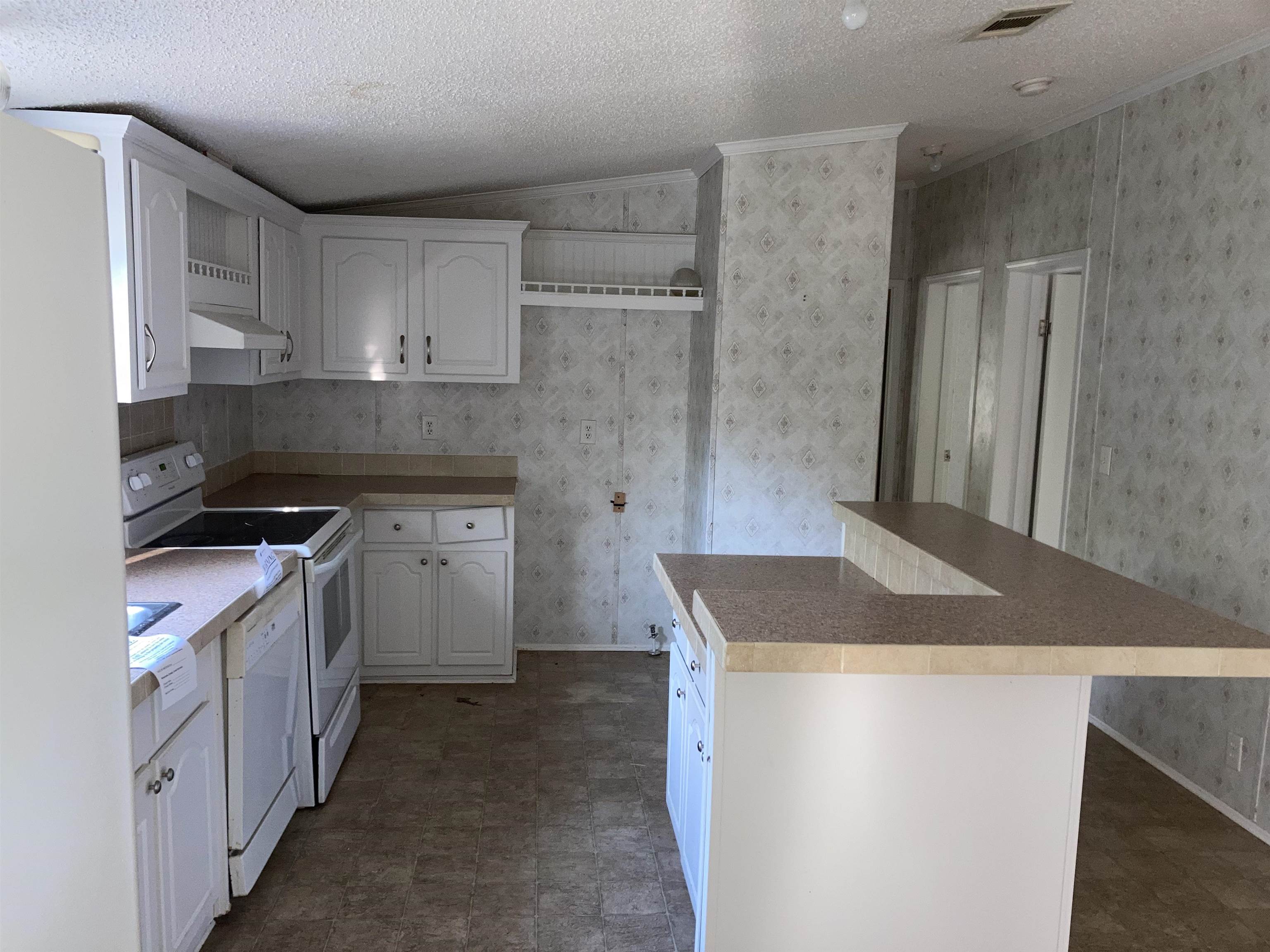 840 Rose Road Somerville, TN 38068 - Photo 14 of 21 Kitchen featuring a textured ceiling, white appliances, white cabinetry, wallpapered walls, and a kitchen breakfast bar