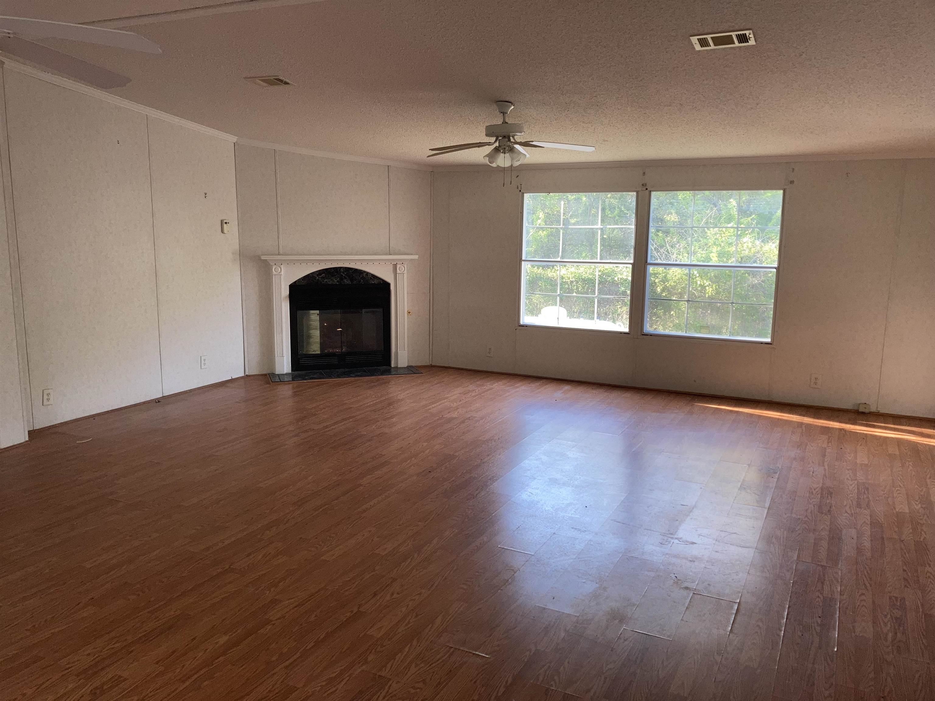 840 Rose Road Somerville, TN 38068 - Photo 9 of 21 Unfurnished living room featuring a ceiling fan, dark wood-style flooring, a fireplace with flush hearth, ornamental molding, and a decorative wall