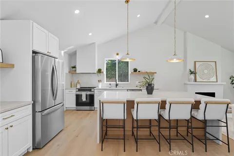 a kitchen with stainless steel appliances a refrigerator a stove a dining table and chairs with wooden floor