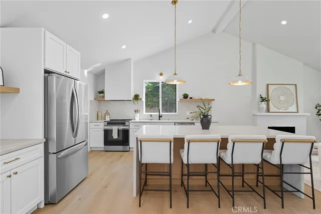 a kitchen with stainless steel appliances a refrigerator a stove a dining table and chairs with wooden floor