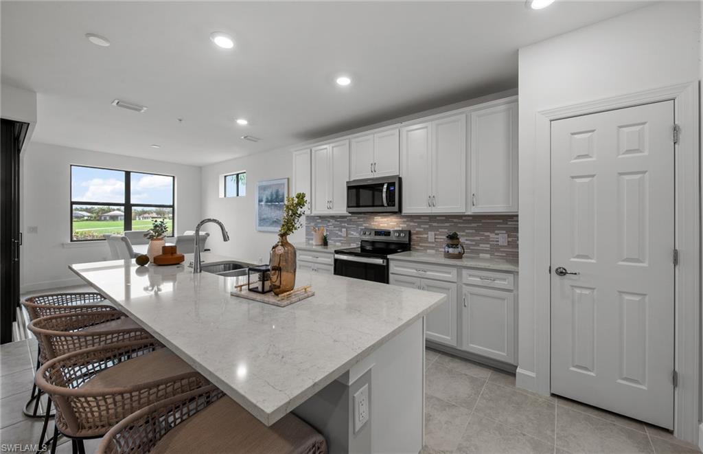 5693 Mayflower Way, Unit 1107 Ave Maria, FL 34142 - Photo 12 of 46 a kitchen with a refrigerator a stove a sink a dining table and chairs