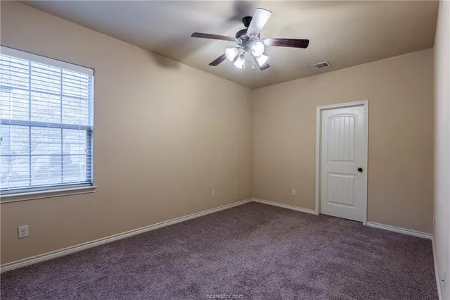 an empty room with chandelier fan and windows