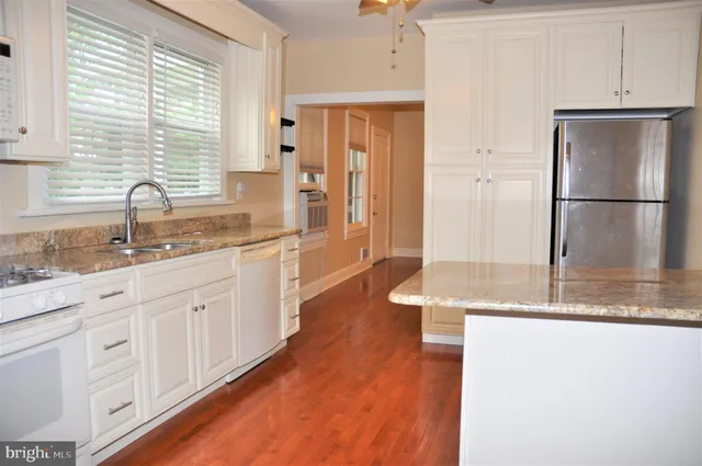 a kitchen with stainless steel appliances granite countertop a refrigerator a sink and white cabinets
