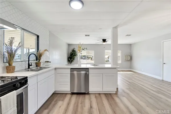 a kitchen with stainless steel appliances granite countertop a stove a sink dishwasher and white cabinets with wooden floor