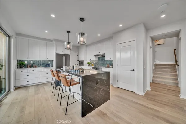 a kitchen with stainless steel appliances kitchen island granite countertop a refrigerator a stove a sink dishwasher and white cabinets with wooden floor