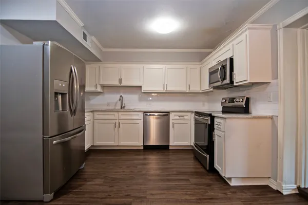 a kitchen with stainless steel appliances granite countertop a refrigerator a stove a sink and white cabinets with wooden floor