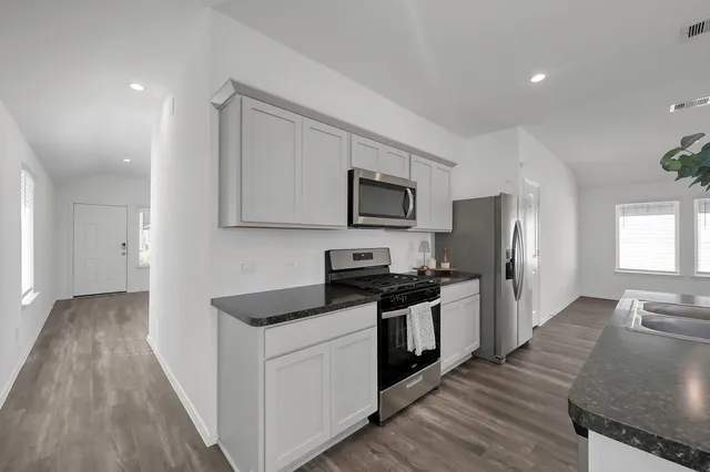 a kitchen with granite countertop a stove top oven a sink dishwasher a refrigerator and white cabinets with wooden floor