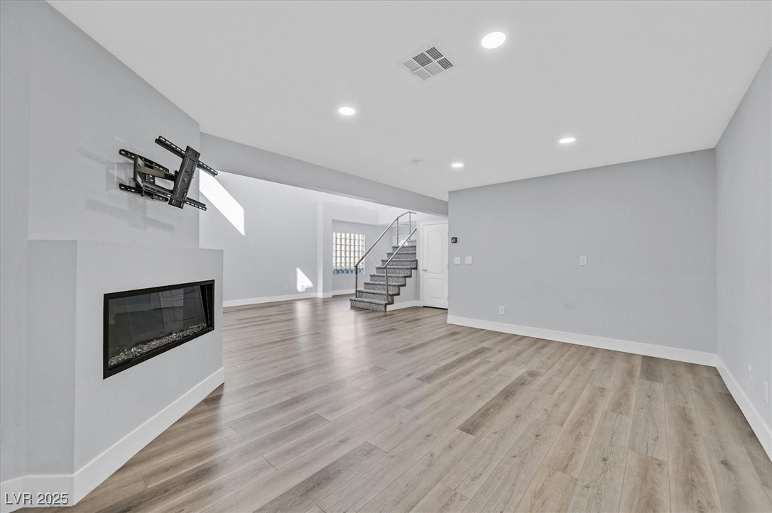 5421 Painted Mirage Road Las Vegas, NV 89149 - Photo 6 of 35 Unfurnished living room with visible vents, a glass covered fireplace, stairway, light wood-type flooring, and recessed lighting