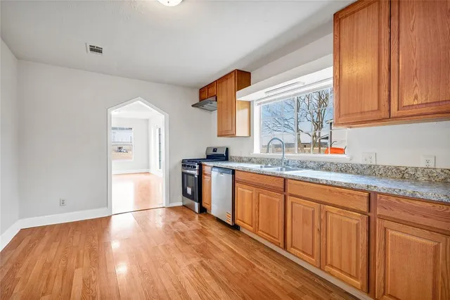 a kitchen with stainless steel appliances granite countertop wooden floors a stove and white cabinets with wooden floor