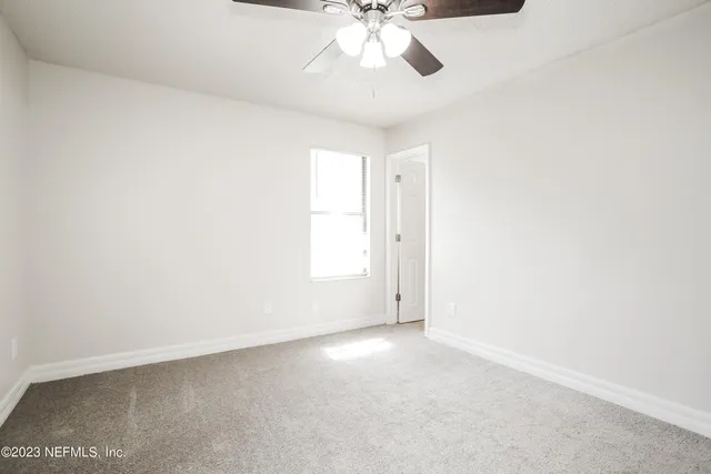 an empty room with a chandelier fan and windows