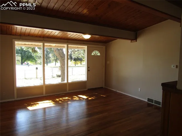 a view of an empty room with wooden floor and a window