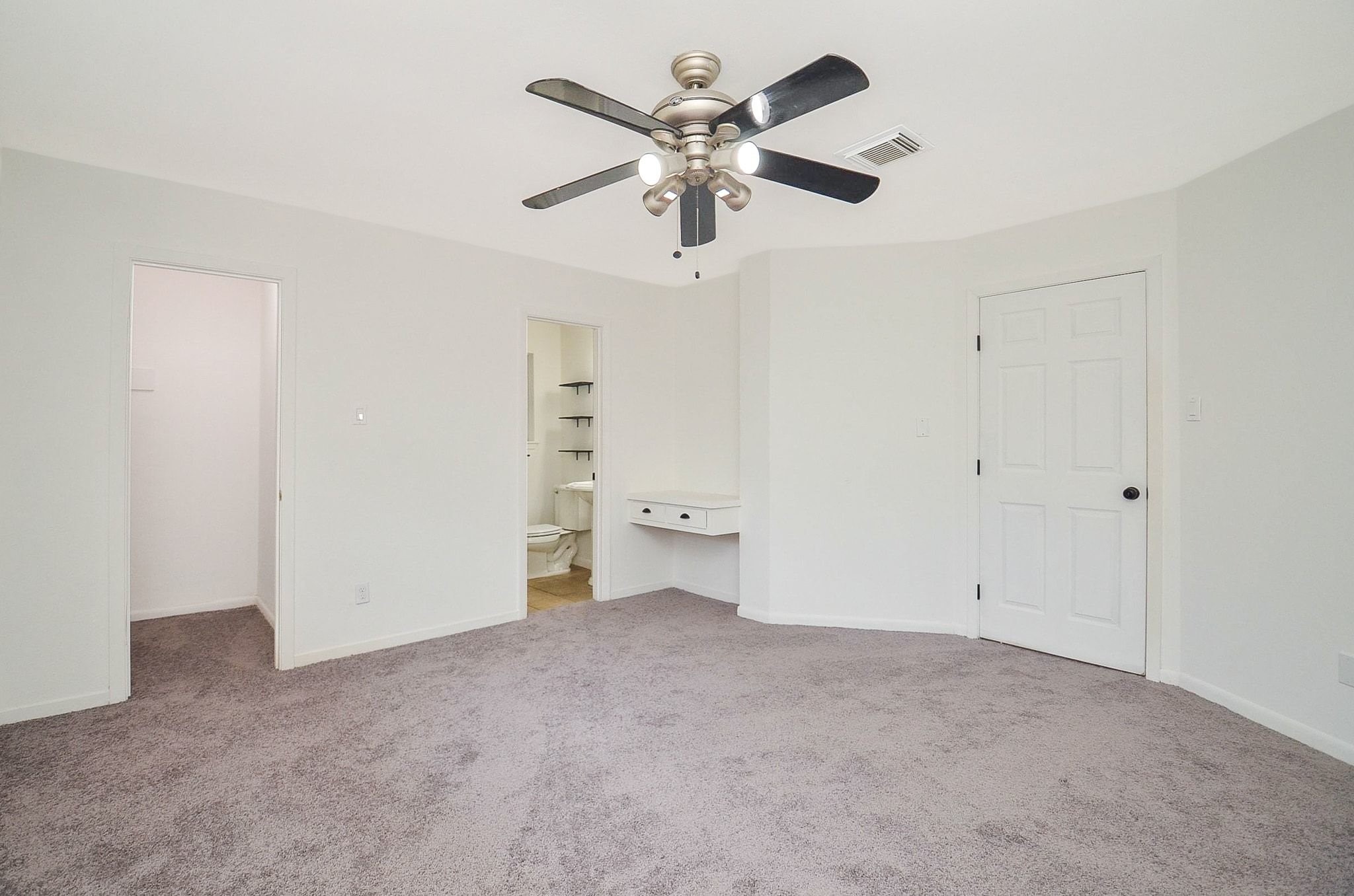 9014 Langfield Road Houston, TX 77040 - Photo 22 of 37 This spacious secondary suite retreat offers fresh neutral paint, plush gray carpeting, and an updated brushed nickel ceiling fan. Designed with convenience in mind, the suite features an ensuite bathroom, a walk-in closet alcove, and a custom built-in floating vanity desk perfect for a makeup station or quiet workspace.