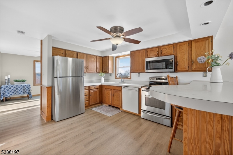 61 Coykendall Road Wantage, NJ 07461 - Photo 5 of 43 a kitchen with stainless steel appliances a refrigerator a stove a sink a microwave a dining table and chairs with wooden floor