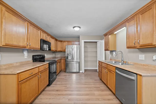 a kitchen with stainless steel appliances granite countertop a stove top oven a sink dishwasher and a refrigerator with wooden cabinets