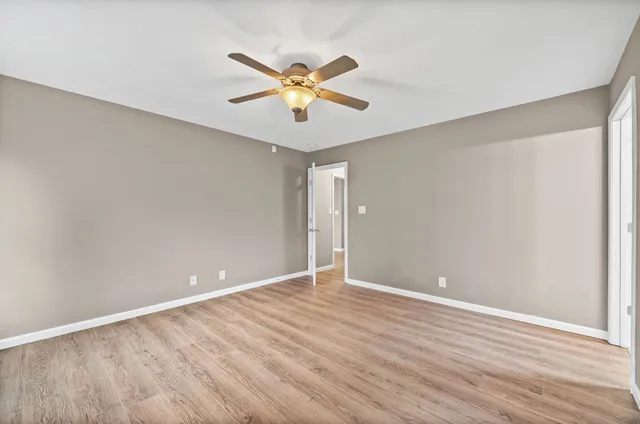 a view of an empty room with wooden floor and a ceiling fan