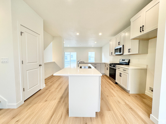 1650 North Main Street Layton, UT 84041 - Photo 9 of 24 Kitchen featuring a central island with an undermount sink, light wood-finish flooring, white cabinetry with dark hardware, stainless steel appliances, and recessed lighting