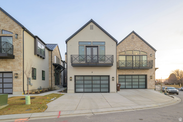 Contemporary home with an attached garage, stucco siding, driveway, a balcony, and stone siding