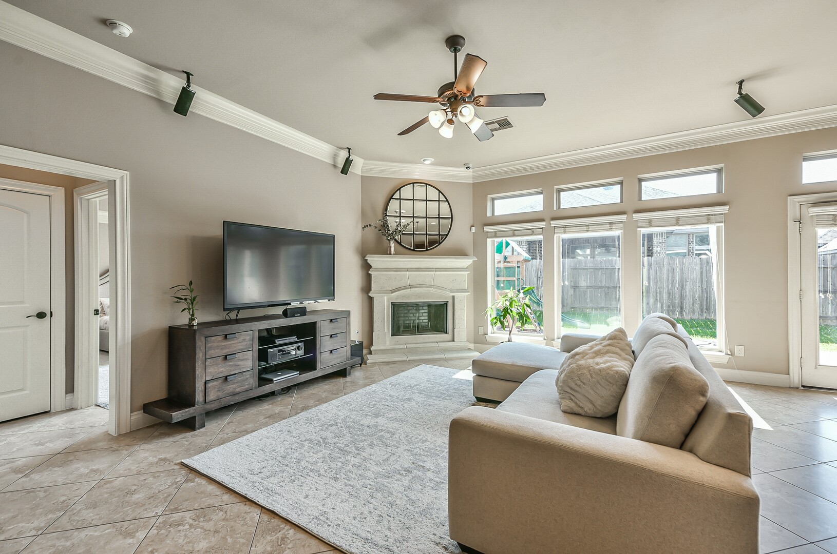 10323 Belvamera Road Richmond, TX 77407 - Photo 7 of 25 Spacious living room with natural light, featuring a ceiling fan and a cozy fireplace. Neutral tones and large windows create a bright, inviting atmosphere.