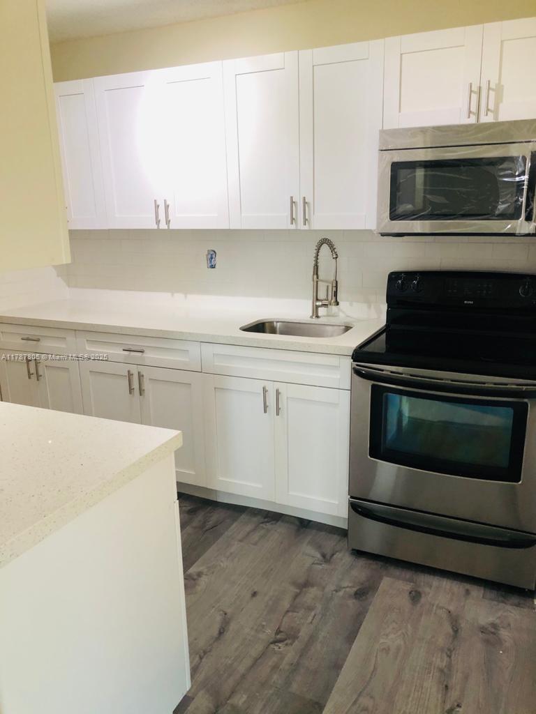 451 Northeast 207th Lane, Unit 102 Miami, FL 33179 - Photo 2 of 8 a kitchen with sink a microwave and cabinets