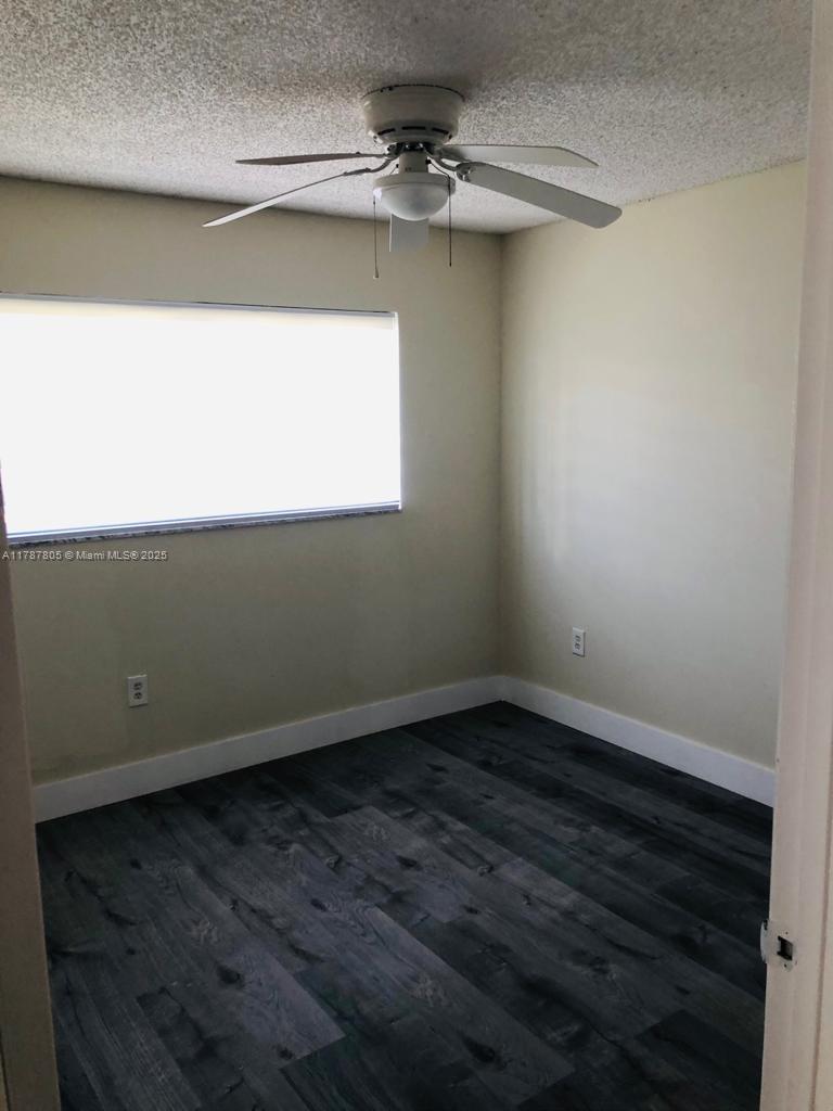 451 Northeast 207th Lane, Unit 102 Miami, FL 33179 - Photo 5 of 8 an empty room with a ceiling fan and wooden floor