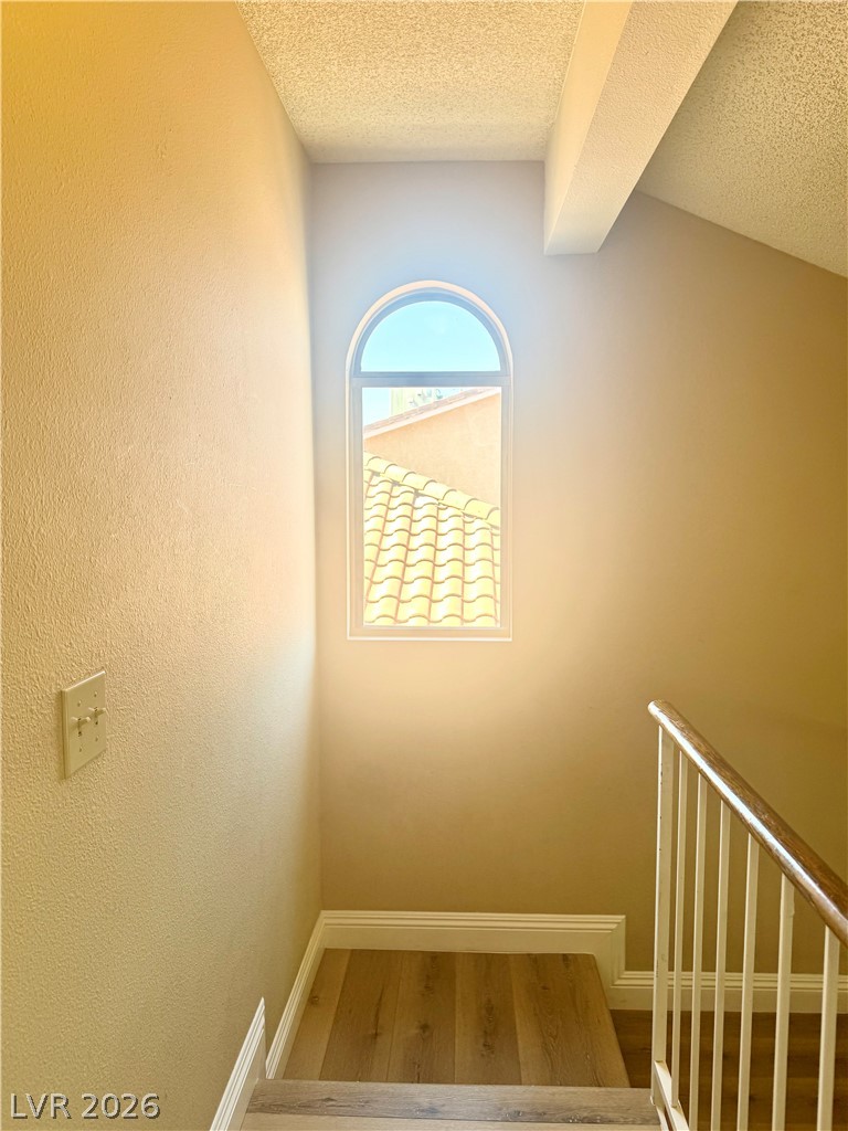 135 Primero Way Henderson, NV 89074 - Photo 9 of 15 Natural light streams through an arched window, illuminating the elegant wooden staircase with a classic railing.