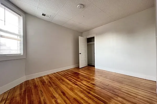 a view of an empty room with wooden floor and a window