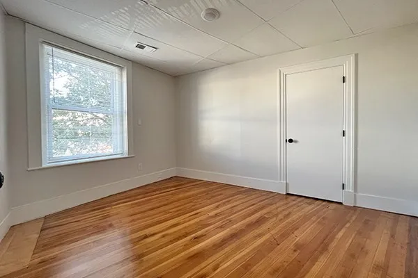 a view of an empty room with wooden floor and a window