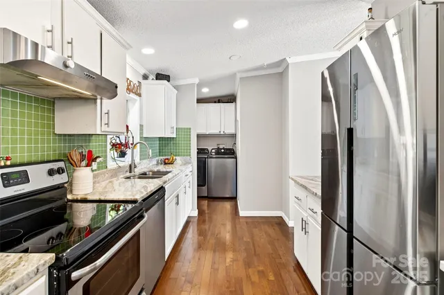 a kitchen with kitchen island granite countertop a refrigerator a sink dishwasher a stove and white cabinets with wooden floor