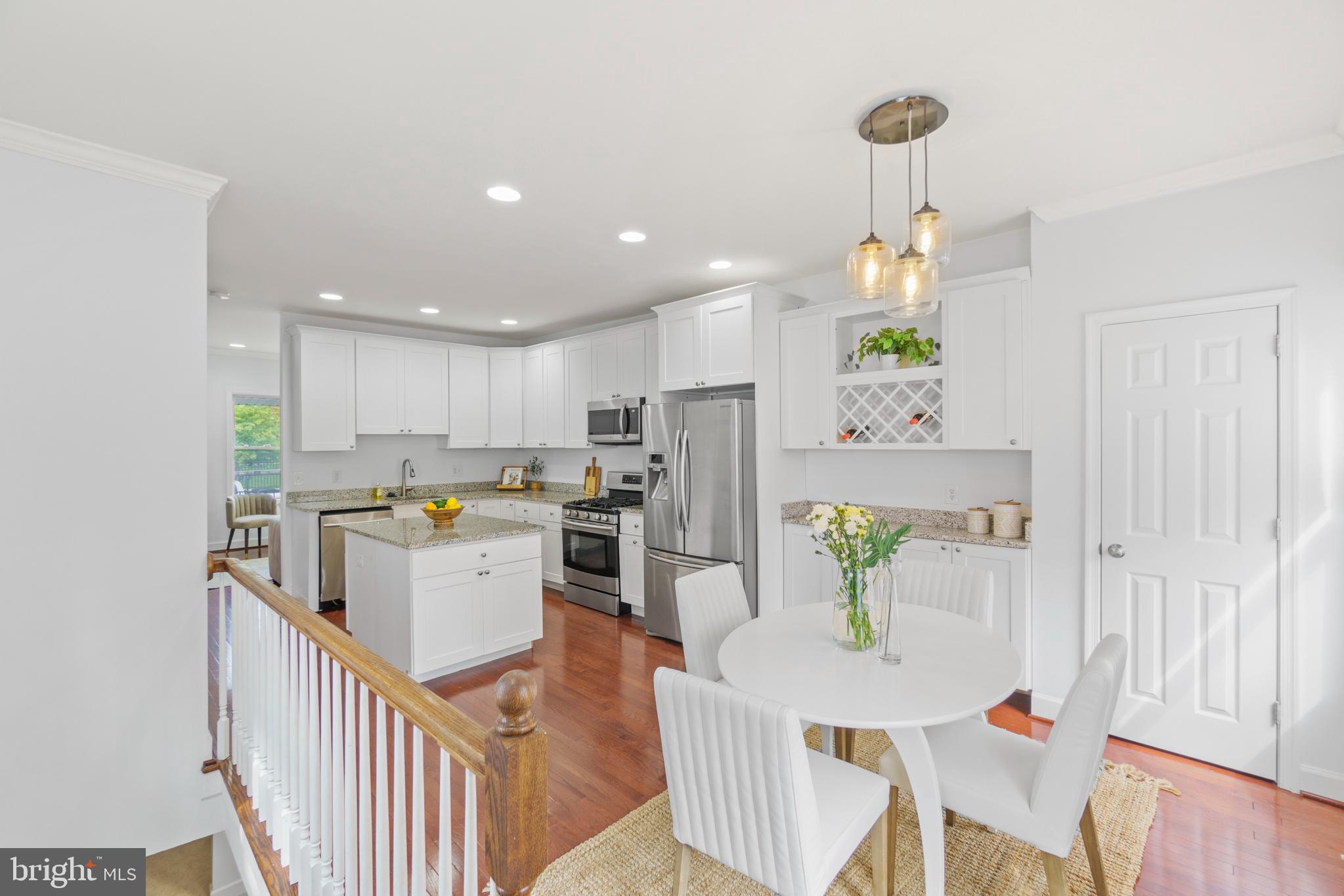a kitchen with stainless steel appliances kitchen island granite countertop a refrigerator a stove top oven a dining table and chairs with wooden floor