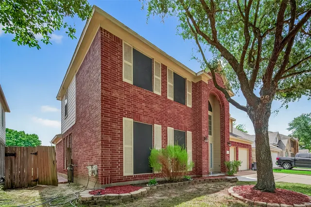 a view of a house with brick walls plants and large tree