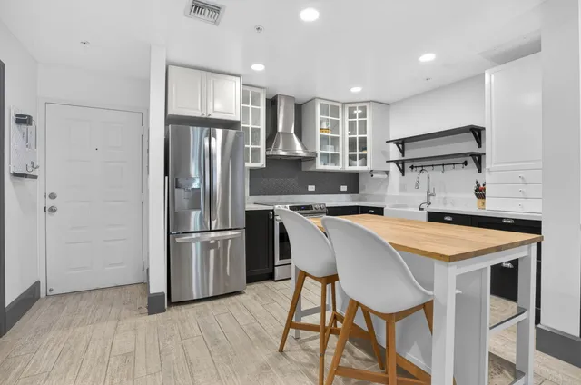 a kitchen with stainless steel appliances granite countertop a refrigerator a sink dishwasher a stove and white cabinets with wooden floor