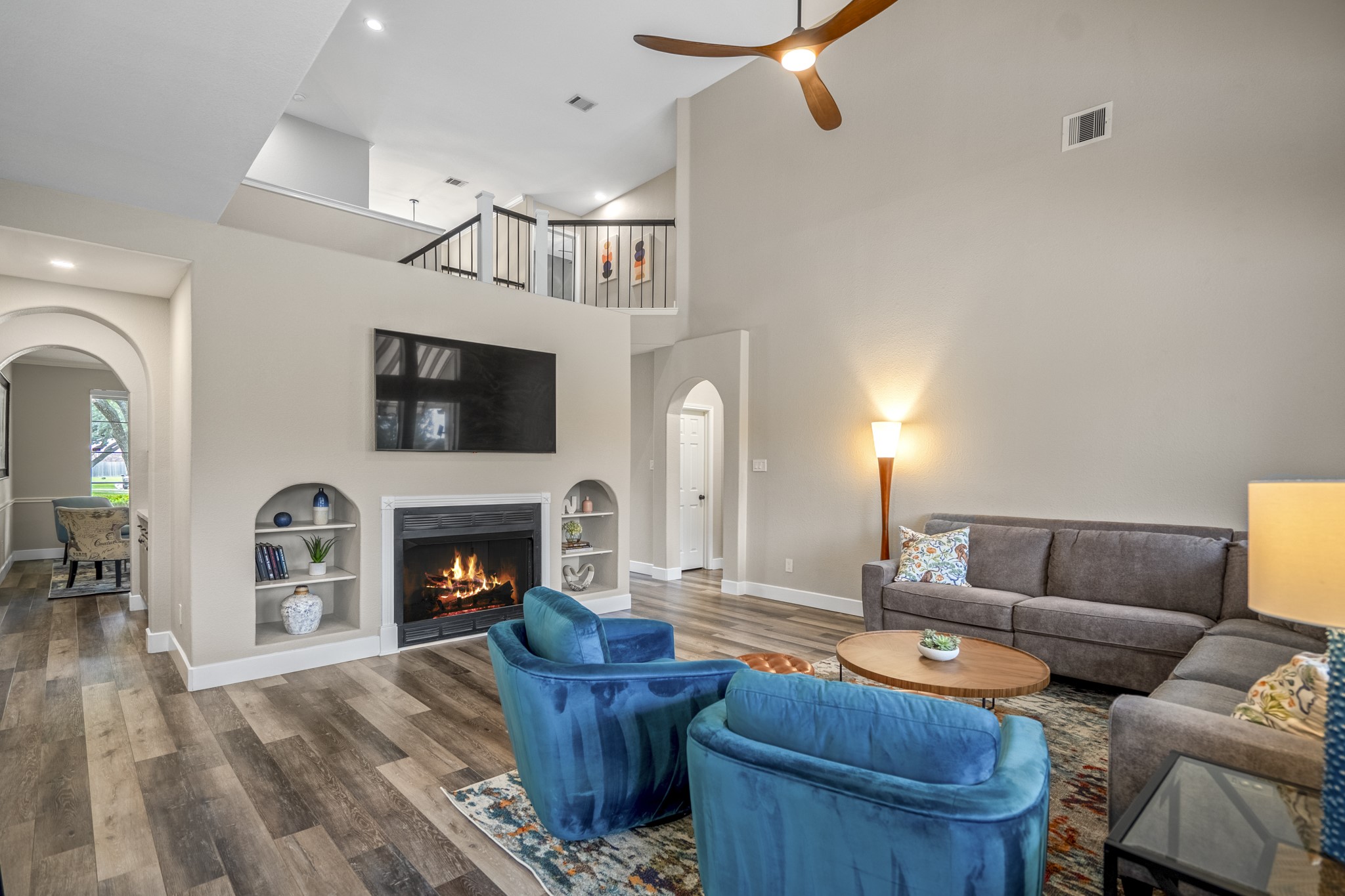 5835 Pinelake Crossing Drive Spring, TX 77379 - Photo 17 of 50 As you move back into the living space from the kitchen, the vaulted two-story ceiling and open-to-above design continue to define the room, carrying the same bright, connected feel seen from the initial view. The fireplace with built-in niches anchors the space with subtle architectural detail, while the upstairs game room overlooks from above. Just beyond, the arched doorway near the fireplace leads into the private primary suite.