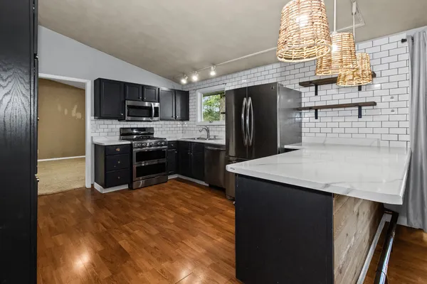 a kitchen with stainless steel appliances granite countertop a sink a stove a refrigerator cabinets and a dining table