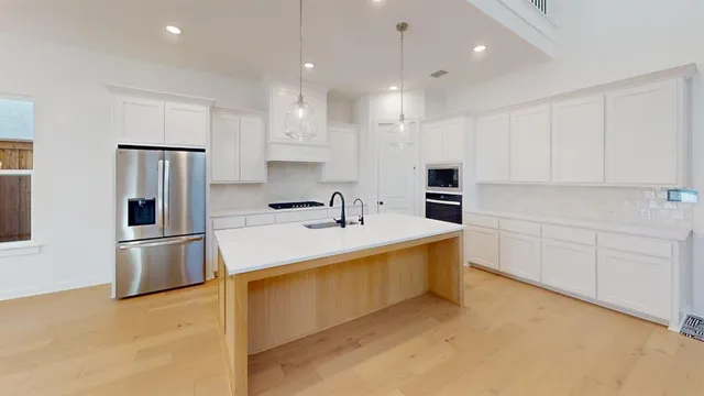 a large kitchen with stainless steel appliances granite countertop a sink a stove a refrigerator and white cabinets