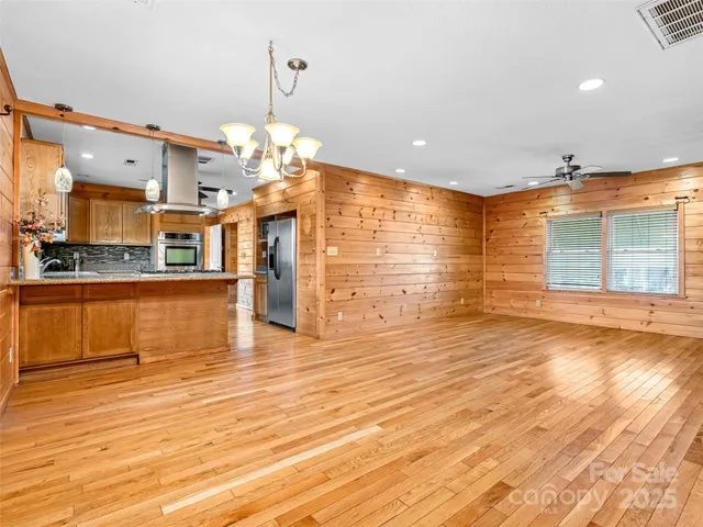 a view of a living room with kitchen island stainless steel appliances wooden floor and chandelier