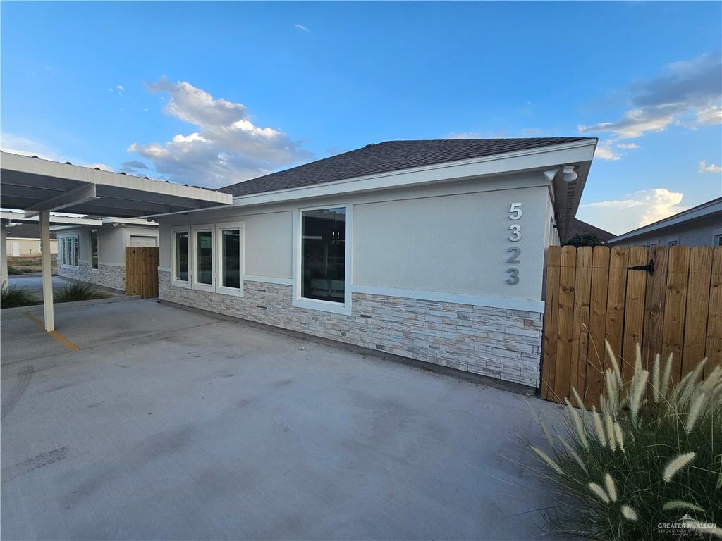 5323 Vision Street Rio Grande City, TX 78582 - Photo 4 of 16 View of home's exterior featuring stone siding, a patio area, roof with shingles, and stucco siding