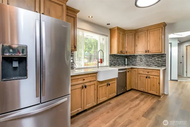 a kitchen with stainless steel appliances granite countertop a refrigerator a sink dishwasher a stove with wooden cabinets and wooden floor