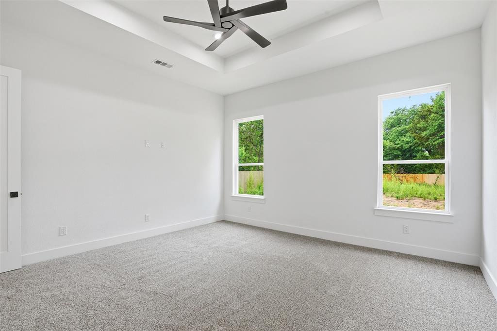 1111 Riverwood Road Dallas, TX 75217 - Photo 32 of 40 Spacious room featuring a contemporary ceiling fan, tray ceiling, two large windows, and plush grey carpeting