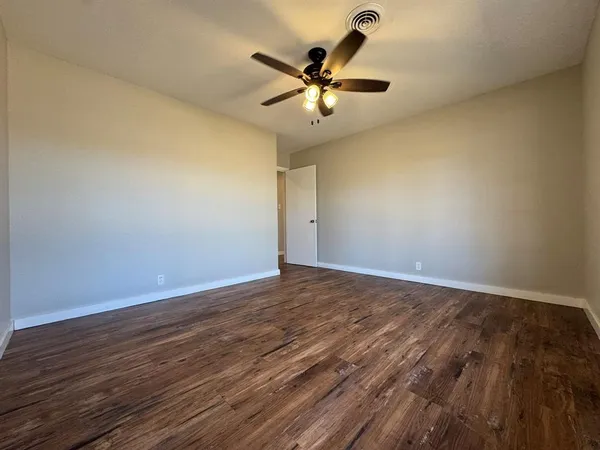 a view of an empty room with wooden floor and a ceiling fan