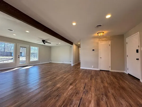 a view of an empty room with wooden floor and a window