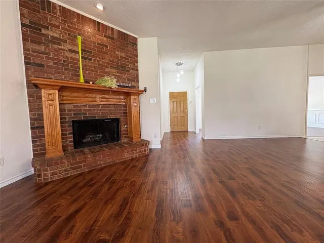 a view of an empty room with wooden floor fireplace and a window