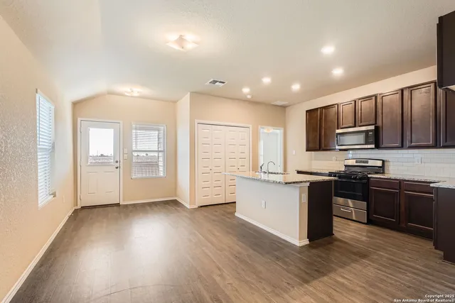 a kitchen with stainless steel appliances granite countertop a stove top oven a sink dishwasher a refrigerator and a microwave oven on the wooden floor