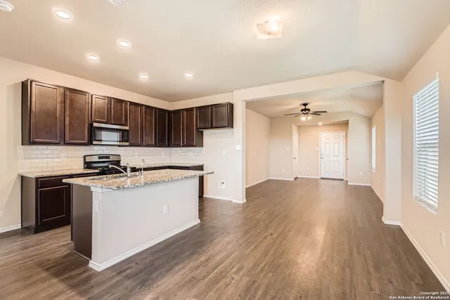 a kitchen with stainless steel appliances granite countertop a stove top oven a sink dishwasher a refrigerator and a microwave oven on the wooden floor