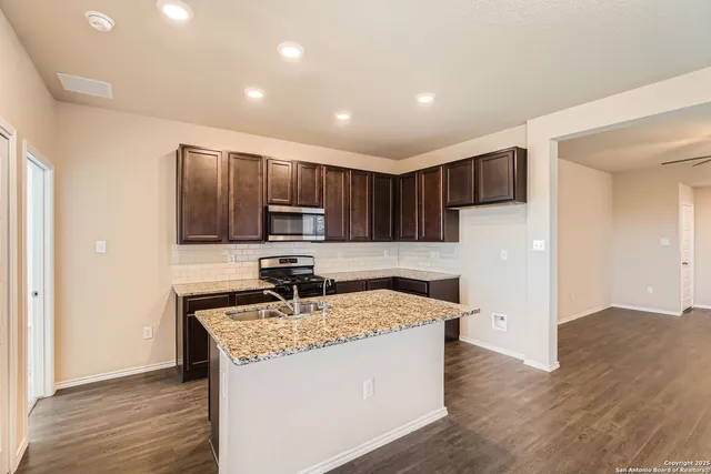 a kitchen with kitchen island granite countertop stainless steel appliances a stove refrigerator sink and microwave