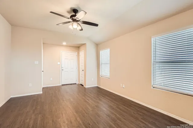 a view of an empty room with wooden floor and a ceiling fan