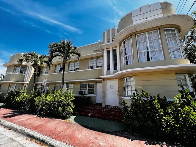 a front view of a multi story residential apartment building with yard and parking