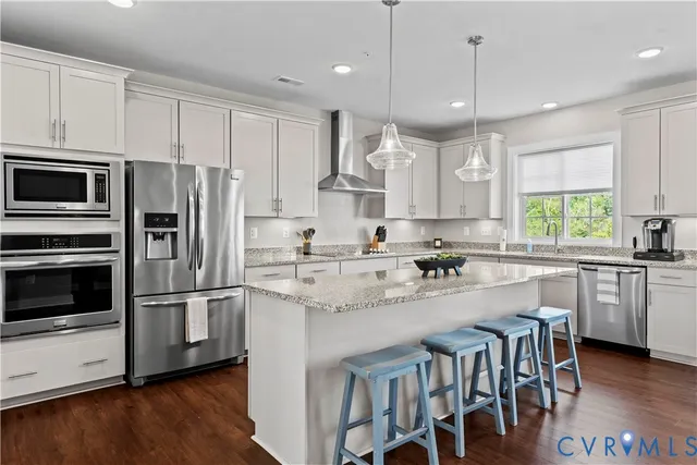 a kitchen with stainless steel appliances granite countertop a refrigerator a stove a sink a dining table and chairs with wooden floor