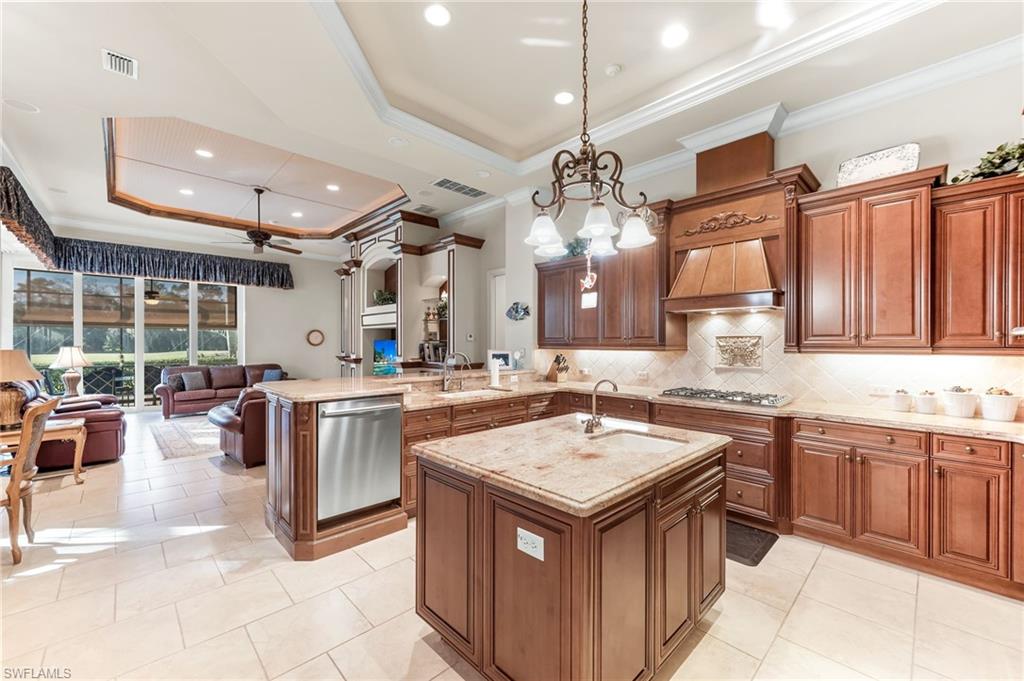 7615 Palmer Court Naples, FL 34113 - Photo 12 of 50 Kitchen with a tray ceiling, ornamental molding, wood finish cabinets, a peninsula, and pendant lighting