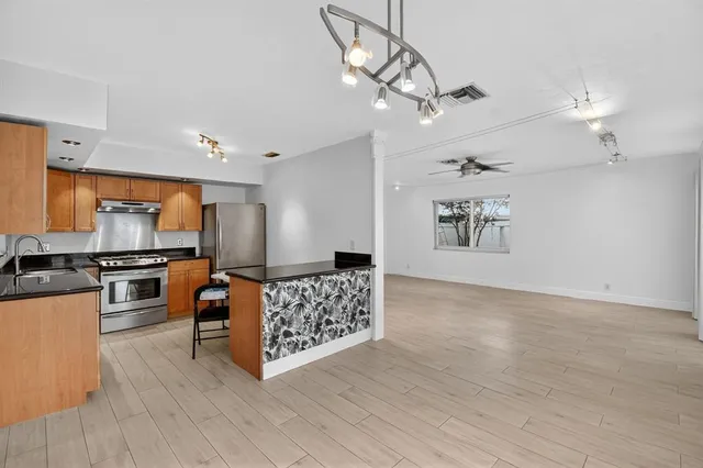 a kitchen with stainless steel appliances a stove top oven a sink dishwasher and a refrigerator with wooden floor